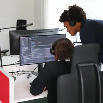 Zwei Denkströme Mitarbeitende arbeiten im Büro an der TYPO3-Website-Entwicklung und prüfen Quellcode am Monitor.