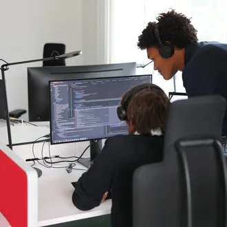 Zwei Denkströme Mitarbeitende arbeiten im Büro an der TYPO3-Website-Entwicklung und prüfen Quellcode am Monitor.