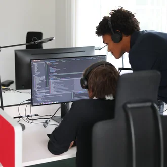 Zwei Denkströme Mitarbeitende arbeiten im Büro an der TYPO3-Website-Entwicklung und prüfen Quellcode am Monitor.