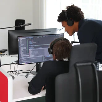 Zwei Denkströme Mitarbeitende arbeiten im Büro an der TYPO3-Website-Entwicklung und prüfen Quellcode am Monitor.