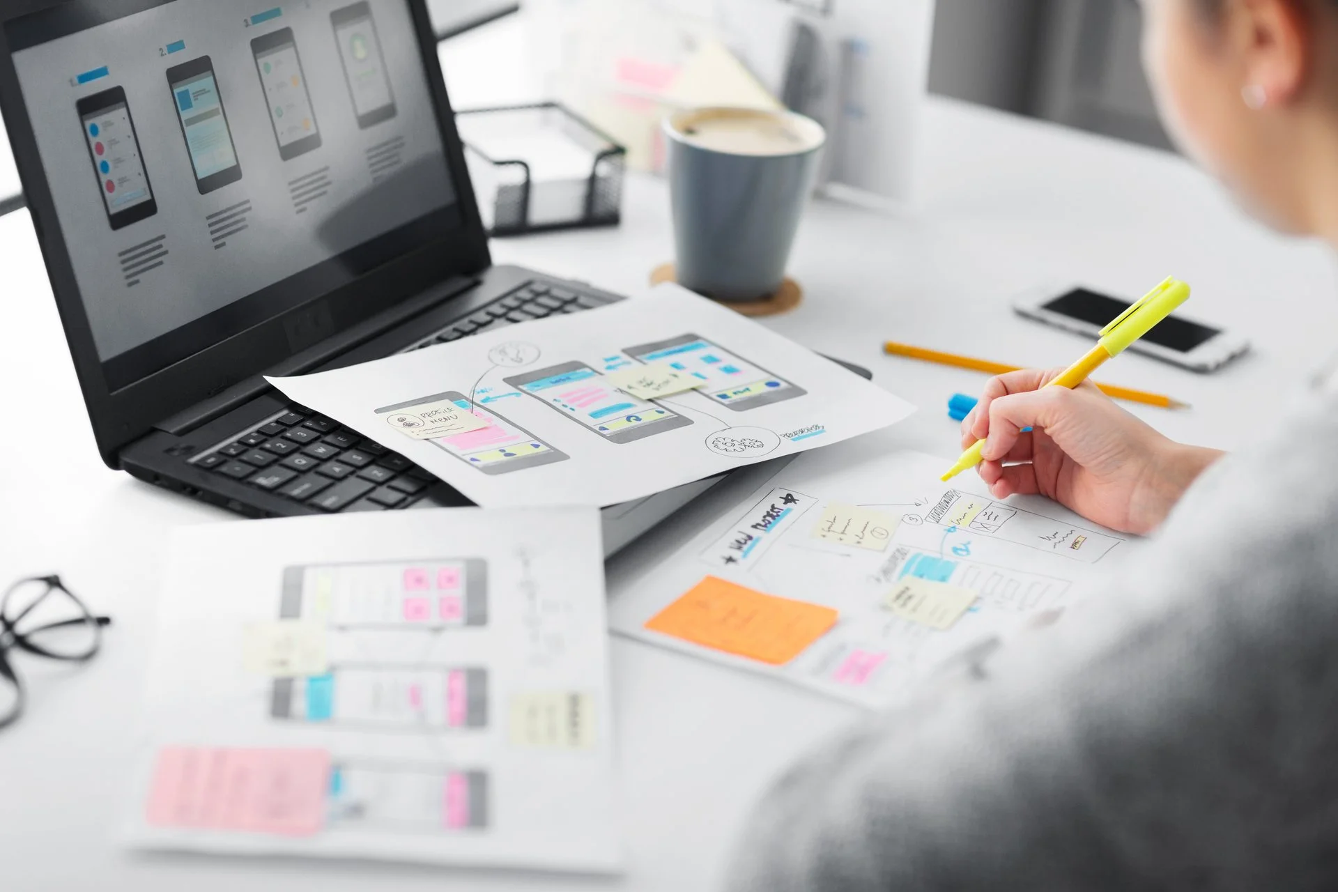 UX-Designerin entwickelt Wireframes und mobile App-Prototypen mit Skizzen und Laptop – kreative Konzeptarbeit im digitalen Produktdesign