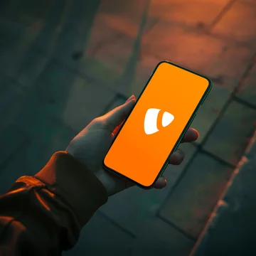 Hand hält Smartphone mit orangefarbenem Bildschirm und TYPO3-Logo, fotografiert bei Dämmerlicht auf dunklem Gehweg – symbolisiert Content-Management, Webentwicklung und mobile CMS-Nutzung