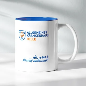 Weiße Kaffeetasse mit blauem Innenrand, Logo des Allgemeinen Krankenhauses Celle und Slogan „... da, wenn’s darauf ankommt!“ auf heller Fläche