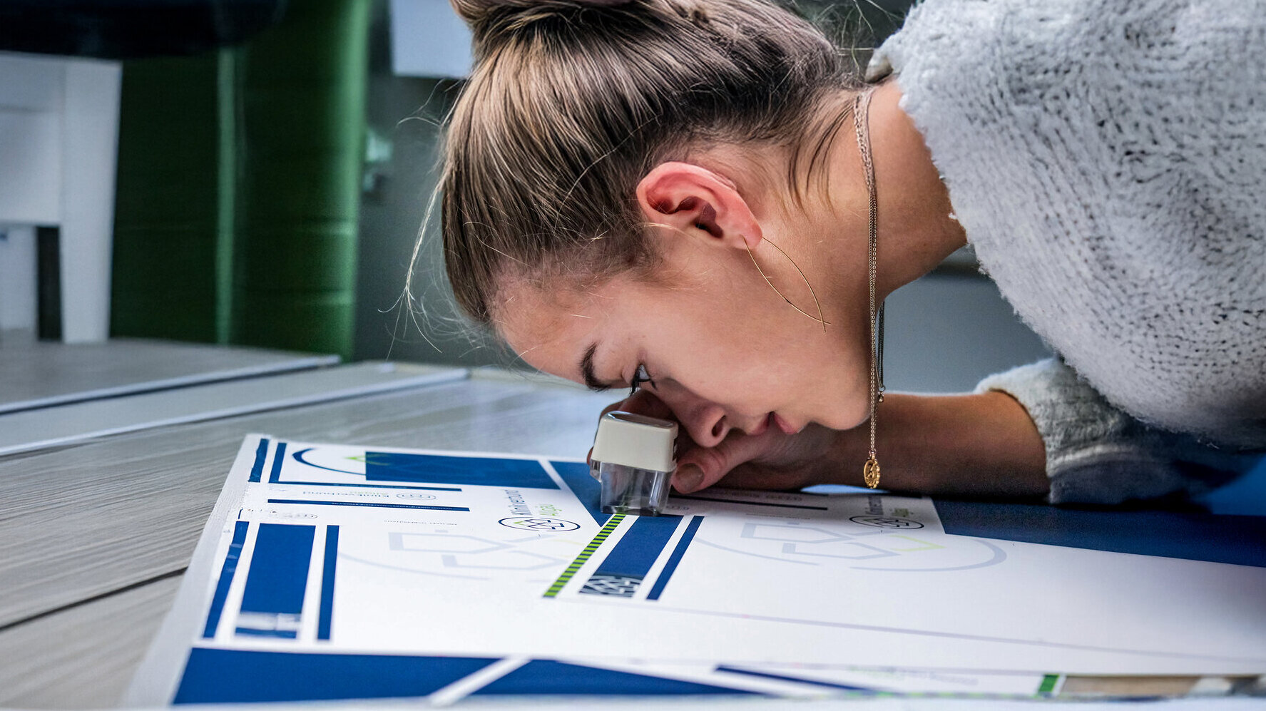Mitarbeiterin prüft sorgfältig einen Druckbogen mit Lupe – Detailaufnahme eines kreativen Produktionsprozesses im Bereich Markenkreation bei der Denkströme