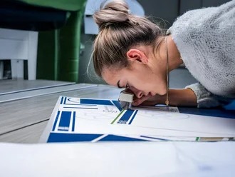 Mitarbeiterin prüft sorgfältig einen Druckbogen mit Lupe – Detailaufnahme eines kreativen Produktionsprozesses im Bereich Markenkreation bei der Denkströme