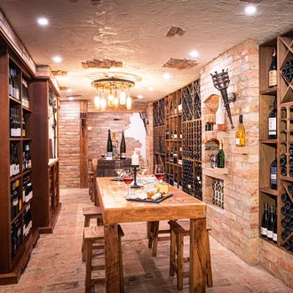 Stimmungsvoller Weinkeller mit rustikaler Ziegelwand, Holzregalen voller Weinflaschen und gedecktem Verkostungstisch mit Käseplatte