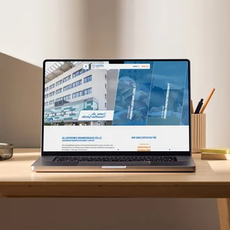 Laptop auf Schreibtisch mit geöffneter Website des Allgemeinen Krankenhauses Celle, Startseite mit Klinikfoto und Navigationselementen sichtbar