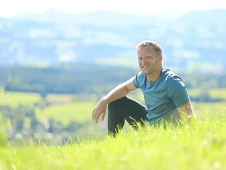 Christian Schoch sitzend auf einer Wiese mit Blick ins Allgäu