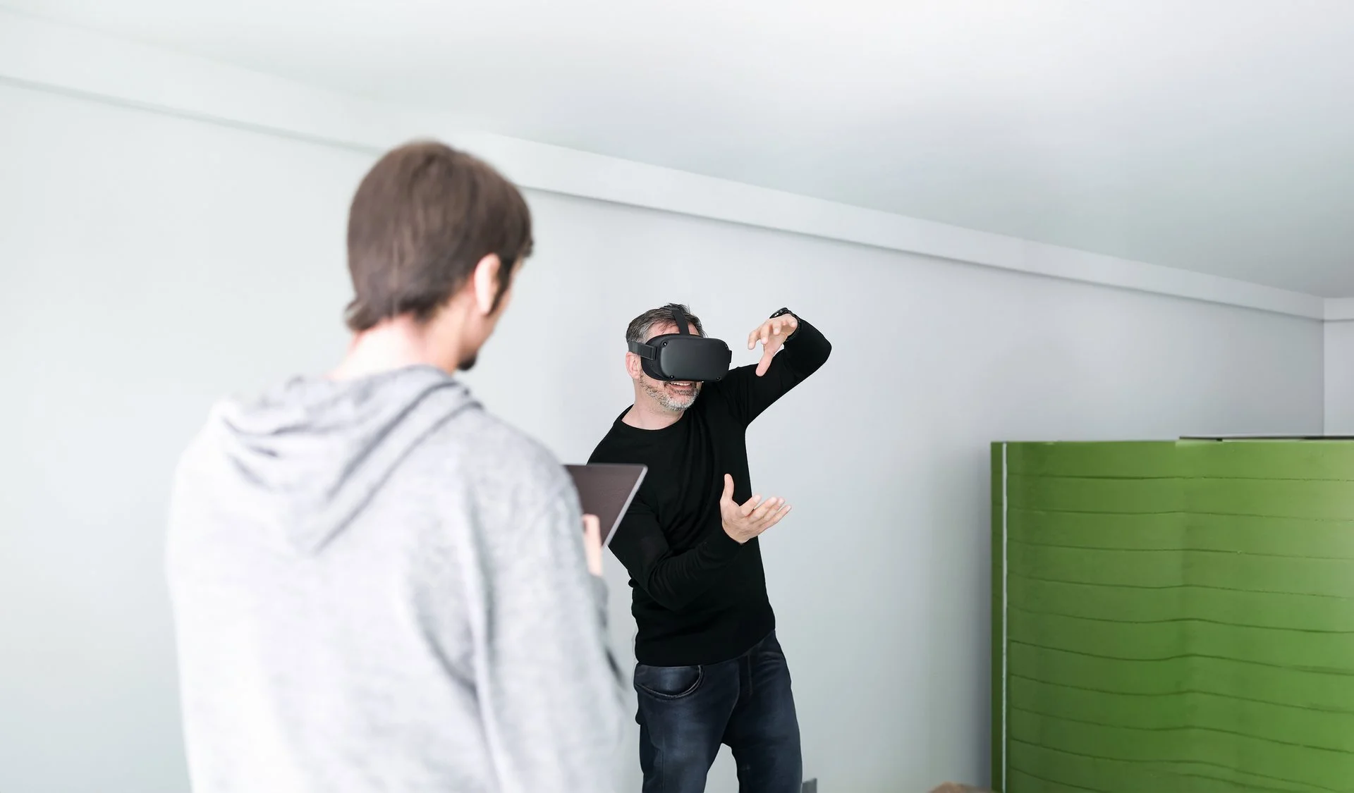 Denkströme IT-Entwickler mit VR-Brille testet virtuelle Realität im Büro der Denkströme Gruppe, betreut von Kollege mit Tablet – Symbol für innovative Digitalentwicklung und immersive Technologien