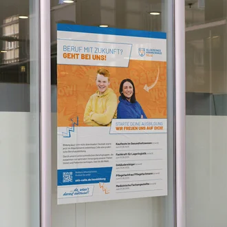 Ausbildungsplakat des Allgemeinen Krankenhauses Celle an Glasfassade mit jungen Menschen, Berufsinformationen und QR-Code zur Bewerbung