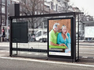 Bushaltestelle mit Citylight-Plakat der Allgäu Pflege und dem Slogan ‚Herzensflüsterer – Mit uns Pflege gestalten‘, zeigt zwei ältere Menschen in vertrauter Geste – emotionale Pflegekampagne zur Fachkräftegewinnung