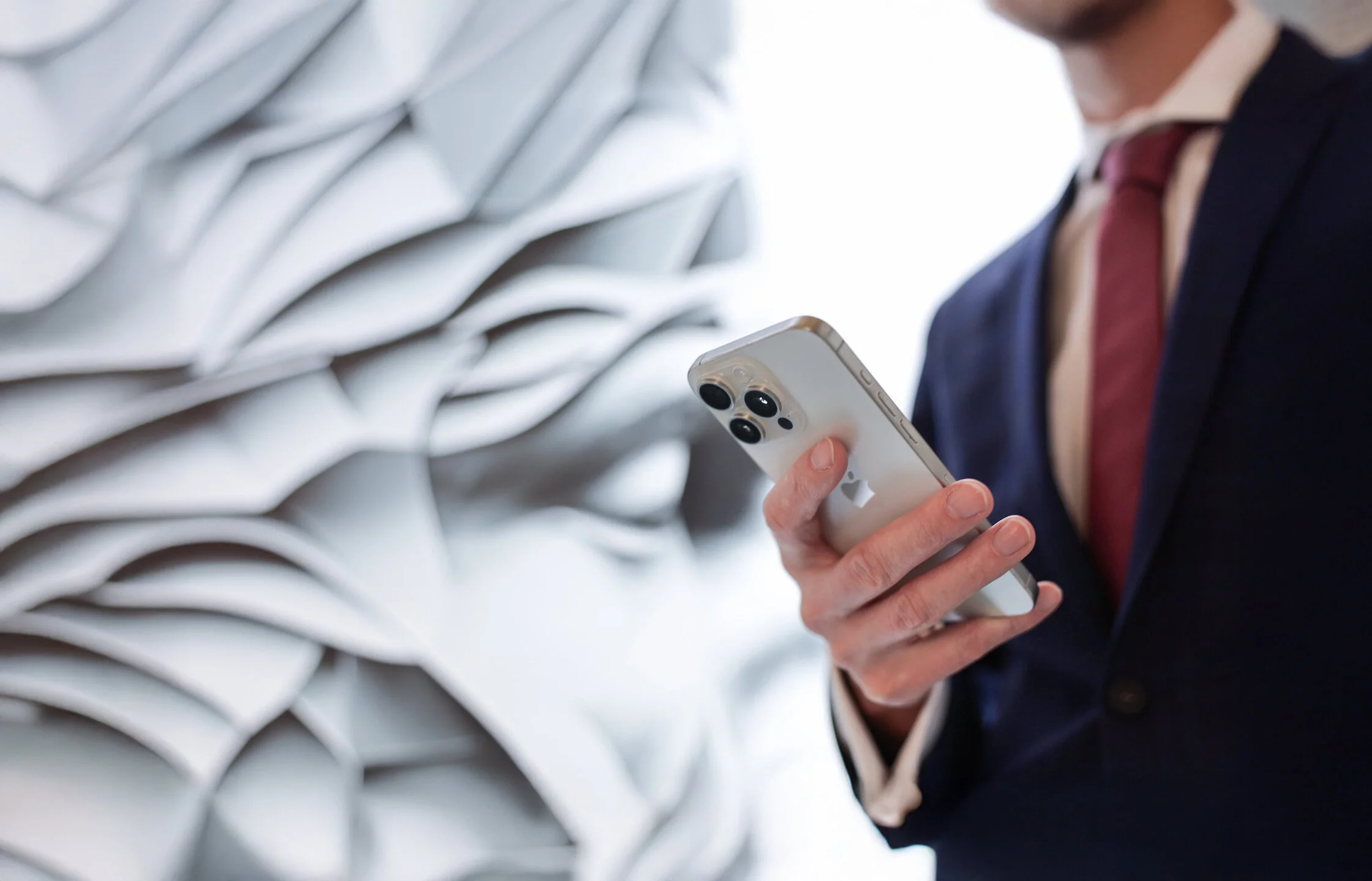 Denkströme Mitarbeiter im Anzug nutzt iPhone zur digitalen Kommunikation vor abstrakter Markenwand der Denkströme Gruppe – Symbol für Digital Development und strategische Digitalisierung