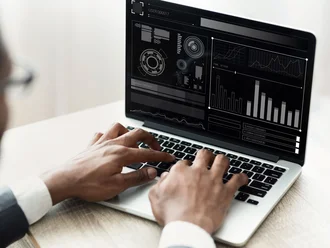 Person arbeitet an einem Laptop mit komplexem schwarzen Dashboard, das Diagramme, Statistiken und digitale Benutzeroberflächen zeigt