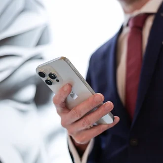 Denkströme Mitarbeiter im Anzug nutzt iPhone zur digitalen Kommunikation vor abstrakter Markenwand der Denkströme Gruppe – Symbol für Digital Development und strategische Digitalisierung