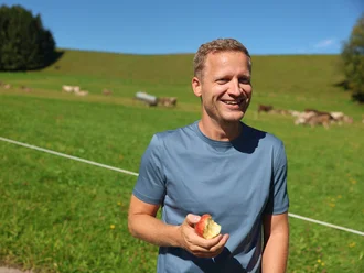 Christian Schoch auf einer Allgäuer Wiese mit Apfel in der Hand