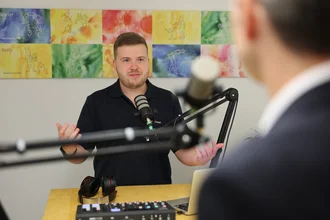Social Media Manager bei Denkströme nimmt einen Podcast auf: Er spricht in ein Mikrofon am Tisch, vor ihm liegen Kopfhörer, Mischpult und Laptop.
