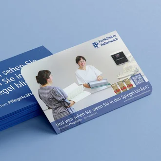 Stapel blauer Visitenkarten mit Pflegekampagnen-Slogan und Vorderseite der Fachkliniken Hohenaurach mit Motiv von Pflegekraft und Bewerberin.