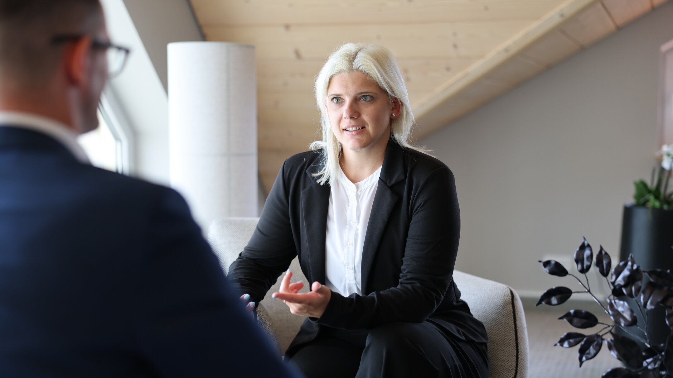 Denkströme Mitarbeiterin im Gespräch mit einem Kollegen im Besprechungsbereich des Büros – Beratungsszene in moderner Arbeitsumgebung.