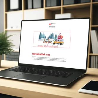 Laptop auf Schreibtisch zeigt digitale Weihnachtskarte des Bayerischen Roten Kreuzes mit der Aufschrift ‚Frohe Weihnachten!‘ und dem Titel ‚Jahresrückblick 2024‘ – digitale Präsentation von BRK-Inhalten in festlichem Kontext