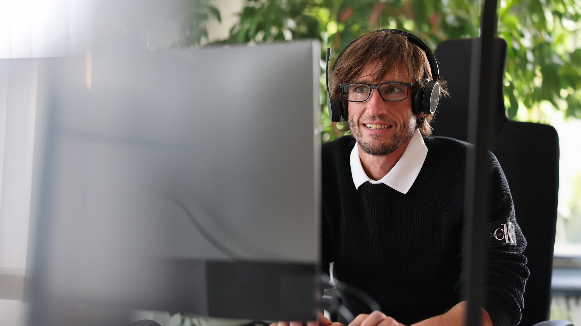 Mitarbeiter bei Denkströme arbeitet mit Headset am Computer; im Hintergrund sind Pflanzen am Fenster zu sehen.
