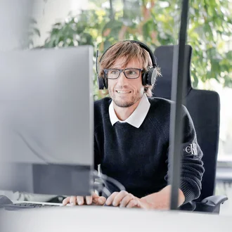Mitarbeiter bei Denkströme arbeitet mit Headset am Computer; im Hintergrund sind Pflanzen am Fenster zu sehen.