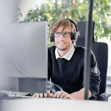 Mitarbeiter bei Denkströme arbeitet mit Headset am Computer; im Hintergrund sind Pflanzen am Fenster zu sehen.