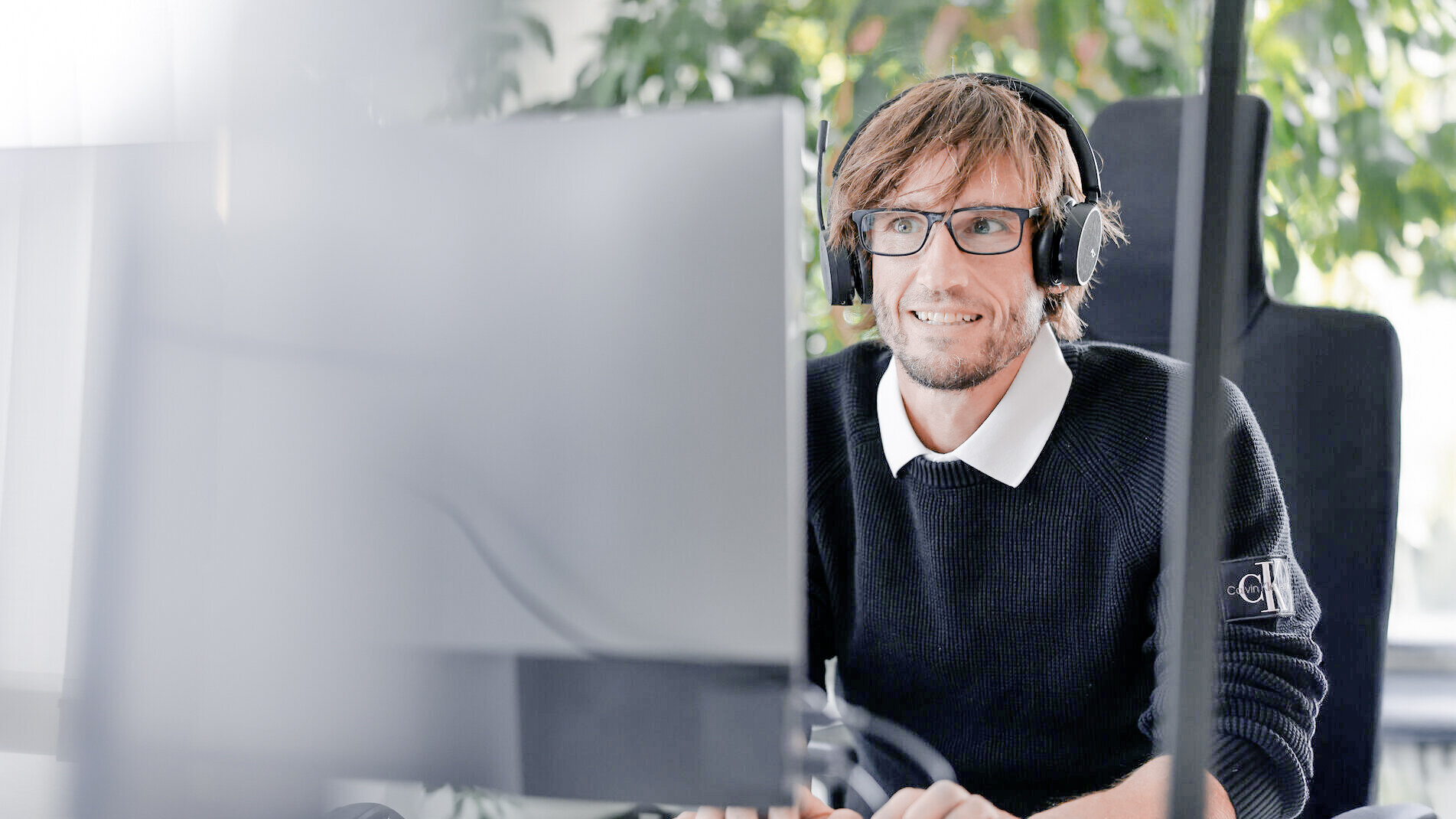 Mitarbeiter bei Denkströme arbeitet mit Headset am Computer; im Hintergrund sind Pflanzen am Fenster zu sehen.