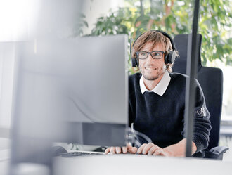 Mitarbeiter bei Denkströme arbeitet mit Headset am Computer; im Hintergrund sind Pflanzen am Fenster zu sehen.