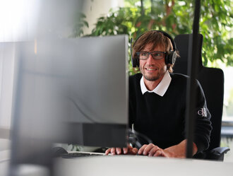 Mitarbeiter bei Denkströme arbeitet mit Headset am Computer; im Hintergrund sind Pflanzen am Fenster zu sehen.