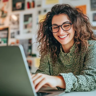 Lächelnde junge Frau mit Brille arbeitet an einem Laptop in kreativ gestalteter Umgebung – steht für moderne Arbeitswelt, Remote Work und inspirierte Produktivität