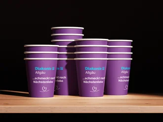 Lila Kaffeebecher der Diakonie Allgäu mit dem Slogan „schmeckt nach Nächstenliebe“