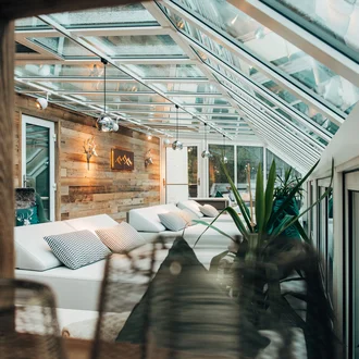 Panoramaliegebereich mit Glasdach, weißen Daybeds, Holzverkleidung und alpiner Dekoration in modernem Wellnesshotel