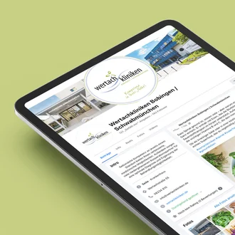 Tablet mit geöffneter Facebook-Seite der Wertachkliniken Bobingen | Schwabmünchen auf grünem Hintergrund. Die Seite zeigt ein Titelbild der Klinik, das Logo „wertachkliniken – regional & kompetent“ sowie einen aktuellen Beitrag mit einem Bild frischen Spinats.