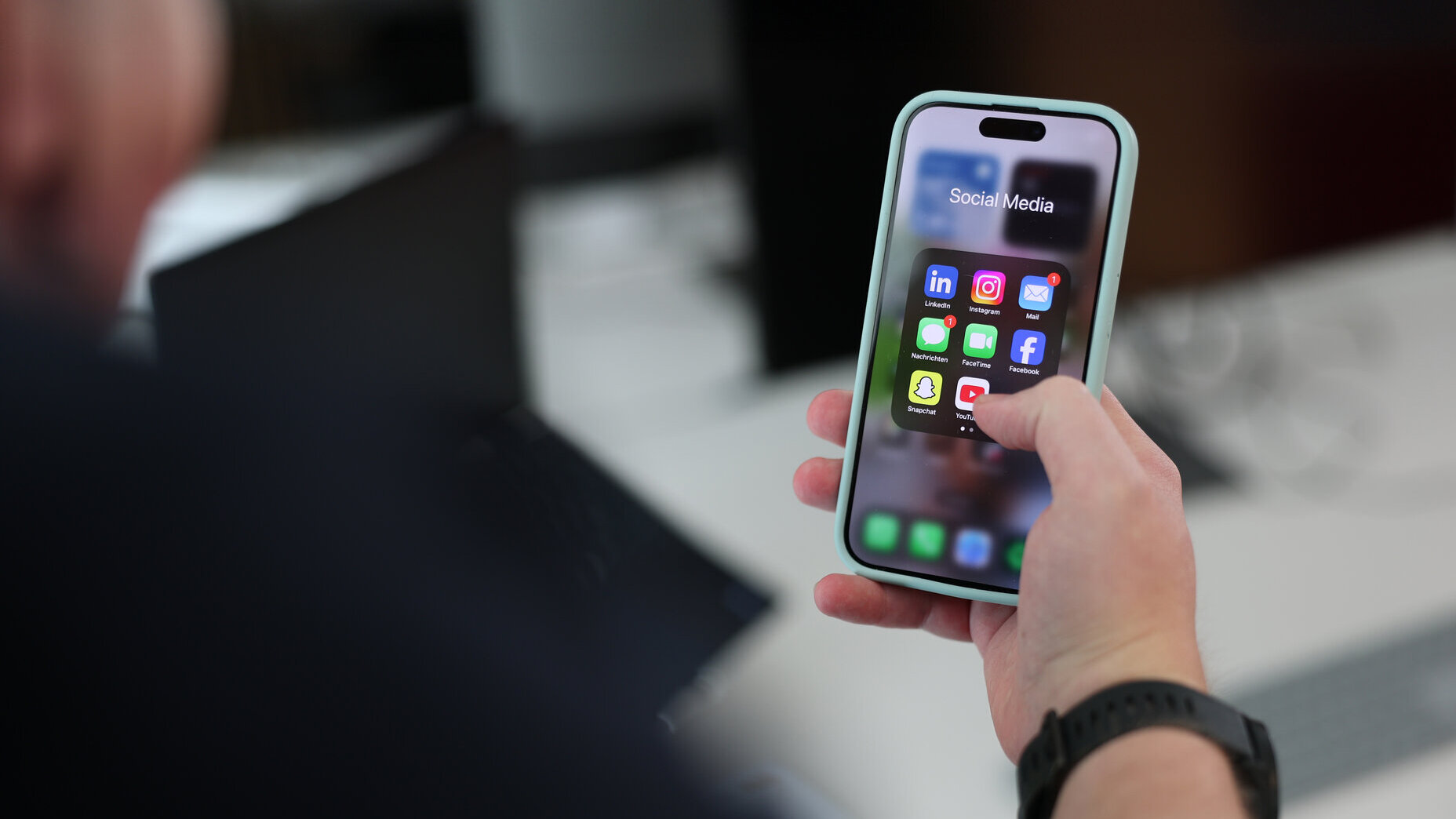 Hand hält ein Smartphone mit geöffnetem Social-Media-Ordner; sichtbar sind App-Icons wie LinkedIn, Instagram, Facebook, TikTok und YouTube.