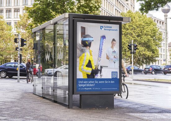 Großflächenplakat der Fachklinik Herzogenaurach mit Pflegekampagne an Bushaltestelle im urbanen Straßenverkehr vor moderner Architektur.