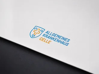 Prägedruck des Logos vom Allgemeinen Krankenhaus Celle in Blau und Orange auf weißem Karton mit modernem, medizinischem Design