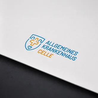 Prägedruck des Logos vom Allgemeinen Krankenhaus Celle in Blau und Orange auf weißem Karton mit modernem, medizinischem Design